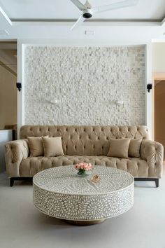 a living room with a couch, coffee table and ceiling fan in front of a stone wall