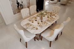a dining room table set with white chairs and place settings for four, surrounded by art work on the wall